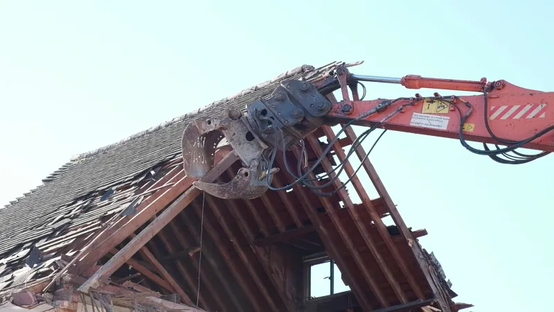 Excavator with a demolition grab pulling the timber rafters out of a pitched roof