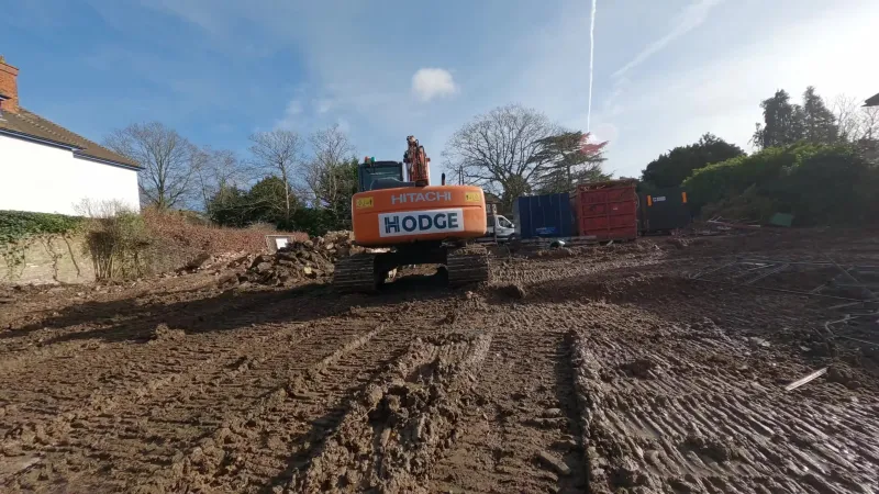 Low view across tracked earth to the back of a Hodge excavator at the far end of a cleared site